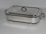 METAL PRATEADO, um (1) suporte com tampa para travessa retangular, liso com alças e pés hexagonais, manufatura WOLFF (tradição desde 1894), linha SOPPIL, medindo 30 x 18 cm; acompanha travessa em vidro, moldado, incolor e translúcido da manufatura MARINEX.