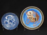 FAIANÇA E PORCELANA, dois (2) pratos decorativos: 1 representando a Deusa Kuan Yin (Deusa da Misericórdia e Compaixão), pintado a mão em policromia sobre fundo na tonalidade azul, borda na tonalidade preta com barrado contínuo, traz marca H dentro de losango e flor de cerejeira, medindo 21 cm diâmetro; 1 ornado na técnica blue and white, representando paisagem lacustre com árvores, pagodes e montanhas, borda com padronização geométrica, marcado em caracteres azul no verso, medindo 16 cm diâmetro.