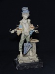 ESCULTURA, uma (1) representando vendedor de guarda chuvas, possivelmente italiana, confeccionada em poliéster policromado, base em mármore negro rajado (com bicados), medindo 25 cm altura.