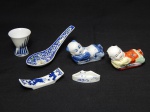 PORCELANA ORIENTAL, seis (6) itens: 2 esculturas na forma de criança deitada, uma policromada e outra na técnica blue and white; 4 apetrechos distintos para degustação na culinária oriental, uma concha, uma taça para saquê (bicada na base), um suporte para hashi e um recipiente para wasabi, medindo a maior peça 12,5 cm comprimento, uma delas com selo vermelho em caracteres.
