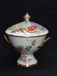 PORCELANA, uma (1) bomboniere com tampa, pega da tampa na forma de peão, possui alças, ornamentação policromada com parras de uva e cerejas, arremates a ouro, sem marca de manufatura aparente, pintada a mão pelo Atelier HELENA REGINA, medindo 21 cm altura.