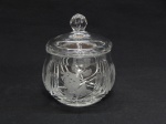 CRISTAL, uma (1) bomboniere com tampa, incolor e translúcida, moldada em sulcos com detalhe floral em satinê, fundo em dália, pega na forma de baga com reentrâncias na parte superior, medindo 15 cm altura.