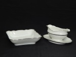 PORCELANA, dois (2) itens: 1 travessa quadrangular, borda recortada com frisos prateados, medindo 20 x 20 cm; 1 molheira com presentoir acoplado, medindo 22,5 x 14 x 9 cm, manufatura Carl Tielsch (fundada em 1845, na cidade de Altwasser, como Carl Tielsch & Co, no inicio suas peças eram marcadas com as letras TPM Tielsch-Porzellan-Manufaktur; em 1917 mudou para Carl Tielsch & Co. A. G.; em 1932 mudou para Porzellanfabrik Tielsch & Co, Abteilung der C. M. Hutschenreuther A. G.; em 1945 mudou para Polska Fabryka Porcelany Tielsch (território deixou de ser da Alemanha e passou a ser da Polônia); em 1952 mudou para Zaklady Porcelany Stolowej Walbrzych; a partir de 1992 acresceu no ultimo nome da fábrica as letras S.A. Funciona assim até a atualidade).