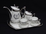 PORCELANA, conjunto tete a tete para café com cinco (5) itens: 1 bandeja; 1 bule; 1 açucareiro e 2 xícaras, ornamentação prateada sobre fundo branco com a legenda BODAS DE PRATA (25 anos) e elementos vegetalistas, manufatura SCHMIDT (Pomerode, SC; Mauá, SP; Campo Largo, PR, fundada em 1945, ainda em atividade, maior fábrica de porcelana da América Latina), medindo a maior peça 27,5 x 16 cm.