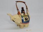 FAIANÇA JAPONESA, um (1) bule modelado na forma de elefante, policromado com predominância da tonalidade amarela, pega da tampa na forma de figura sentada (totalmente no estado com quebrados, colados e perdas, possui partes, não sei se todas), alça em tresse de fibra vegetal, marca de origem na base, possui o craquelê característico do envelhecimento de toda a faiança, medindo 14 cm comprimento.