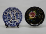 FAIANÇA E FOLHA DE FLANDRES, dois (2) pratos decorativos: 1 pintado a mão com borboletas e flores na técnica blue and white, manufatura LS (Luiz Salvador, destacado mestre da arte de pintura em faiança na olaria de Alcobaça em Portugal, veio para o Brasil e fundou no ano de 1950 uma fábrica em Itaipava, região serrana do Rio de Janeiro, ainda em atividade), medindo 18,5 cm diâmetro; 1 com ornamentação floral policromada sobre fundo negro, sinais de oxidação, medindo 18,5 cm diâmetro.
