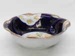 PORCELANA, uma (1) antiga fruteira ou centro de mesa, primeiro quartel do século XX, ornada com rosas em policromia e faixa na tonalidade azul cobalto, generosos arremates a ouro, vazados na borda e relevada em volutas da própria modelagem, possui rachados no fundo da peça, marca usada entre 1903 e 1930, pela manufatura IPF (fundada em 1777 como Furstlich Sachsen Weimar Porzellanfabrik, por Christian Zacharias Grabner, após autozização e empréstimo do Duque Karl August; em 1782 o Duque assume a fábrica e seu secretário Friedrich Johann Justin Bertuchque a gerencia; em 1786 é arrendada para Gotthilf Greiner; em 1792 é arrendada para Friedrich Christian Nonneque; em 1808 a fabrica foi vendida e virou Ilmenauer Porzellanfabrik Nonne & Roesch; em 1836 foi vendida e virou Ilmenauer Porzellanfabrik GmbH; em 1930 após fechamento foi reaberta como Ilmenauer Porzellanfabrik Graf Von Henneberg AG; em 1949 foi nacionalizada e virou VEB Henneberg Porzellan Ilmenau; em 1990 após reunificação alemã virou Graf Von Henneberg Porzellan GmbH; em 2002 virou Neue Porzellanfabrik Ilmenau GmbH, ainda em funcionamento), medindo 26,5 cm diâmetro.