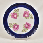 Medalhão de porcelana com larga faixa na borda azul cobalto e centro com rosas sobre fundo branco. Verso marcado.  Apresenta pequeno batido na borda. 37 cm diam