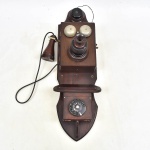 Antigo telefone americano de parede, possivelmente "Ericsson". Caixa em madeira com guarnições em metal e baquelite, campainhas em ferro . (75X25X25)