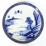 Medalhão em porcelana azul e branca decorado com paisagem. Japão, Meiji, meados do Séc. XIX. 37 cm de diâmetro. (Devido a fragilidade desse lote, seu envio só será realizado através de transportadora especializada).