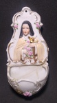 Antigo porta água benta em porcelana Alemã, representando em alto relevo Santa Terezinha de Jesus. Florais pintados a mão. Possui restaura na pia, conforme fotos. Medida: 13 X 6 X 4 cm.
