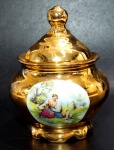 Açucareiro em porcelana decorada por cena galante em policromia e farta pintura em ouro. Mede 12 cm de altura por 9 cm de diâmetro.
