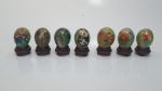 Lindo conjunto com sete ovos decorativos em jade, com diversas pinturas. Acompanham peanhas, medindo 5 cm x 3,5 cm.