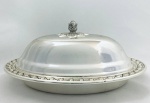 Belíssima manteigueira oval, borda decorada com relevos, pega da tampa em formato de pinha, interior ovalado e removível em demi cristal lapidado. Med. 18,5x13,5x9,5 cm.