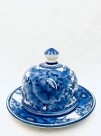 Queijeira com pintura à mão floral em tom azul, em faiança, prato apresenta pequenos desgastes na borda. Med. Alt. 19 cm. Diâm. 27,5 cm.