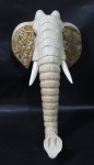 ESCULTURAS - Escultura de parede confeccionada em madeira entalhada representando "Cabeça de Elefante", com rica patinação na tonalidade creme reproduzindo craquelado. Medidas alt 36 cm x larg 21 cm.