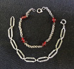 JOIA, duas (02) pulseiras de prata: 1 de elos retos cravados de marcassitas com contrastes portugueses; 1 com corrente denominada cordão baiano, intercalada por contas de vidro vermelho; peso total 13,1grs.