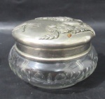 CRISTAL - Um (1) porta jóias / porta pó em cristal lapidado,  com tampa em alúminio adornado com motivos vegetalistas. Medidas: altura 7 cm x 9,5 diâmetro da borda.