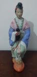 CHINA - Escultura em porcelana, figura feminina de quimono sentada no seat garden, pintada a mão em tons rosa, azul, verde água e alaranjado, meados do séc. xx - Tamanho  17cm x 9,5cm x 6,5cm.