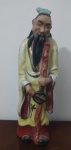 CHINA - Escultura em porcelana, figura Masculina de ancião com cajado segurando leque, numerada na base, pintada a mão em tons vermelho cobre, preto e amarelo, meados do séc. xx - Tamanho  20cm x 6cm x 6,5cm.