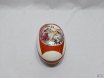 Caixa oval em porcelana com camafeu na tampa. Medindo 17,5cm x 11cm x 11cm de altura. Leve bicado na borda.