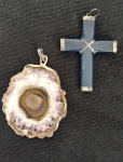 Dois pendentes em cristal de rocha, sendo uma cruz na cor azul e outra peça. As duas circundadas com metal na cor prata, não testado.