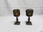 Par de castiçais na forma de cálice em metal adornado com pedras coloridas. Medindo 16,5cm de altura x 7cm de diâmetro de boca.