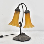 Belíssima luminária de mesa padrão Tiffany estilo Art Noveau elegantemente executado com 2 (duas) luzes, mangas no formato de tulipas em pasta de vidro na cor âmbar, base em bronze com rico trabalho, Impecável estado de conservação. Medida:  35 alt x 26 larg x 22 prof