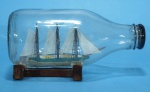 BARCO NA GARRAFA - Miniatura artesanal de veleiro policromado em verde, branco e amarelo, dentro de garrafa, suporte em madeira. 14 cm.