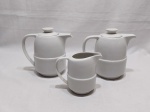 Jogo de servir chá café com 3 peças em porcelana branca, sendo 2 bules e 1 leiteira. Medindo o bule maior 17cm de altura. Um dos bules possui um fio de cabelo na base.