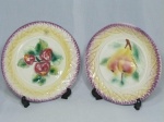 Dois pratos decorativos em porcelana italiana, decorados em alto relevo com frutas, fitas e perolados na borda, pintados a mão. Localizados no fundo. Diam. 20cm.