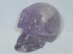 Pedra roxa esculpida e lapidada na forma de crânio. Pequenos sinas de impacto. Med. 8,5 x 12 x 6cm.