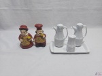 Par de galhetas e saleiro com bandeja em porcelana Schmidt e par de suportes para colher de pau na forma de cozinheiros em porcelana. Medindo a galheta 12,5cm de altura.