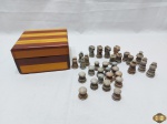 Caixa em madeira marchetada com 32 peças de xadrez em pedra sabão. Medindo o rei 5cm de altura e a caixa 14,5cm x 14,5cm x 8cm de altura. Pequenos bicados nas peças.