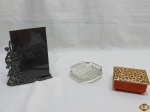 Lote composto de caixa em porcelana, porta retrato em metal e cinzeiro facetado em vidro incolor. Medindo a caixa 10,5cm x 9cm x 5cm de altura.