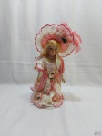 Antiga boneca com cabeça de porcelana, vestida em trajes típicos, com pedestal em resina. Medindo 37cm de altura. Com restauro no rosto.