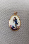 JOIA SACRA, um (1) pingente em porcelana retratando imaginária policromada de Nossa Senhora da Conceição, formato oval, virola, olhal e argola em OURO amarelo de teor abaixo de 750 milésimos, medindo 18 x 13 mm mais olhal e argola.