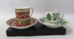 PORCELANA VISTA ALEGRE PORTUGAL - Duas xícaras, de coleção, com seus respectivos pires, em porcelana portuguesa vitrificada branca, sendo uma apoiada sobre suporte em metal dourado, decoradas com largas faixas, guirlandas de folhas e motivos vegetalistas nas tonalidades laranja, verde e dourada, alças vazadas, bordas filetadas a ouro, marcados no fundo. Medidas da maior: alt 6 cm x diam 5,3 cm/ pires: diam 11,5 cm; medidas da menor: alt 4,8 cm x diam 5,3 cm/ pires: 11,3 cm.