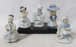 ESCULTURAS - Cinco bibelôs confeccionados em porcelana vitrificada e policromada, representando figuras de "Meninas" em diversas atividades, ricamente trabalhados e arrematados com resquícios dourados. Medidas: maior: alt 12 cm x diam da base 5,8 cm/ menor: 10 cm x larg da base 6,5 cm.