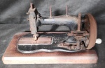 Antiga máquina de costura com pátina preta e  de coleção, no estado,  com movimentação por manivela e engrenagem com caixa de bancada de madeira. Med.20cm x 38 cm