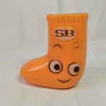 COFRE / COFRINHO sorridente, formato de uma meia / bota. Feito em plástico, nunca foi usado. Acima do rosto sorridente existem as letras SB. Mede aprox. 10 cm de altura.