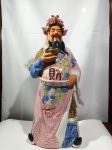 Escultura em porcelana chinesa com vestimentas em rica policromia e adornos multicoloridos sobre a cabeça, medindo: 63cm de altura e 25cm em sua base.