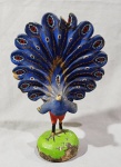 ARTE POPULAR, uma (1) representando pavão azul, confeccionada em barro com policromia, possui quebrados, colados, perdas e defeitos, medindo 25 cm altura.