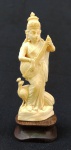 MARFIM, uma (1) escultura representando uma Deusa do Panteon de Deuses Hindú, tocando um instrumento de cordas com pavão aos pés, sinais de raspagem abaixo do braço (possível intervenção), base em madeira, altura total 13,5 cm.