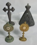 Quatro antigos souvenir religiosos em metal sendo dois ostensorios medindo 6,5cm,  uma Cruz com base em formato de concha  para pendurar chaves medindo 9cm e imagem de Nossa Senhora Aparecida medindo 8cm ( apresenta um pequeno quebrado na base).