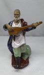 Estatueta em porcelana de um músico oriental,  tocando pipa um instrumento de cordas típico chinês, ricamente detalhada, medindo 22cm de altura.