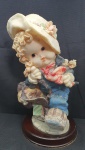 Escultura em resina representando uma criança indo à escola ricamente detalhada, com base em madeira circular, medindo 26cm de altura por  13cm de diâmetro