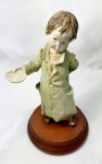 Estatueta em resina representando um pedinte bem detalhada, com base em madeira, medindo 17cm de altura por 9,5cm de diâmetro.