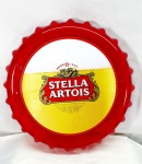 Quadro no formato de tampa de garrafa em plástico rígido,na cor vermelha, com imagem  da Cerveja Stella Artois , para amantes da Boa Cerveja.Stella Artois é uma cerveja belga com mais de 600 anos de tradição. Criada originalmente como presente de Natal para os habitantes de Leuven, na Bélgica, a receita da Stella produz uma cerveja de cor cristalina, aroma suave e notas maltadas, medindo 24cm de diâmetro.