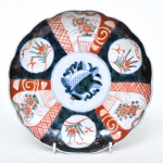 Medalhão em porcelana japonesa "Imari", séc. XIX, esmaltado com ramos e flores com predominância rouge de fer. Borda gomada e ondulada. . Medida: 21,5cm de diâmetro.